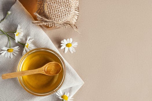 Chamomile syrup in a small bowl and in a jar and chamomile flowers on a linen kitchen towel, copy space.