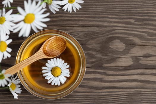 Chamomile syrup in a small bowl and in a jar in the patio on a wooden table.
