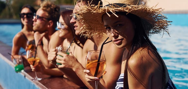 Talking and drinking. Group of young happy people have fun in swimming pool at daytime.