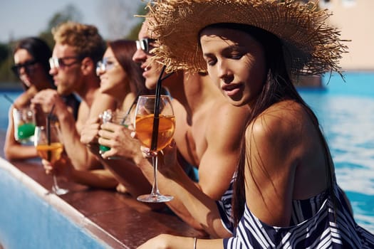 Talking and drinking. Group of young happy people have fun in swimming pool at daytime.