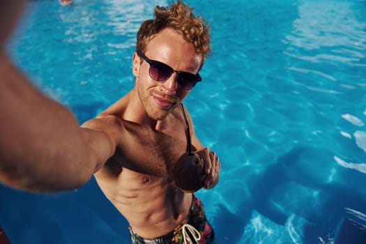 Positive young man have a rest outdoors in swimming pool at daytime.