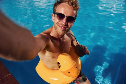 Positive young man have a rest outdoors in swimming pool at daytime.