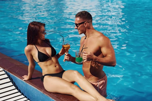 With cocktails. Cheerful couple or friends together in swimming pool at vacation.
