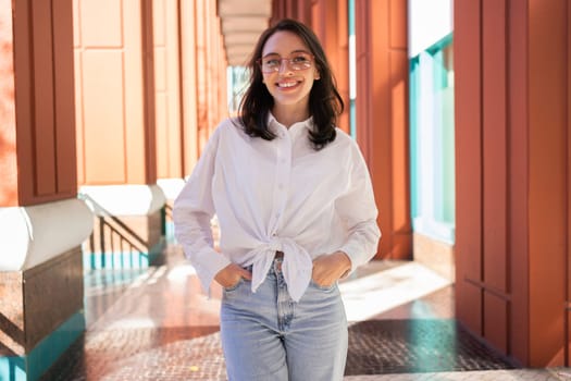 Successful smiling business woman wearing eyeglasses hands in pocket. Modern businesswoman smile standing outdoor dressed white shirt and jeans. Business woman happy positive emotions