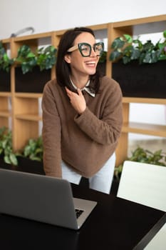 Woman Wearing Glasses using Laptop. Charming businesswoman in eyeglasses and casual clothes working with laptop computer standing looking side. Elegant business female positive emotion vertical shoot