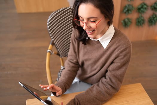 Woman using tablet computer sitting at her desk high angle view. Modern technologies and communication. Young female person studying or working online on touch pad looking at screen device.