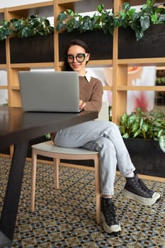 Woman Wearing Glasses using Laptop. Charming businesswoman in eyeglasses and casual clothes working with laptop computer watching screen. Elegant business female full length vertical shoot