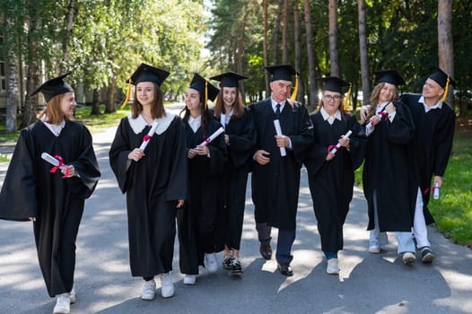 A group of graduates in robes with diplomas in their hands walk outdoors. Elderly student