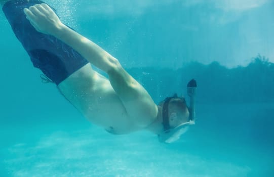 Side view of man that swimming underwater in the pool at daytime.