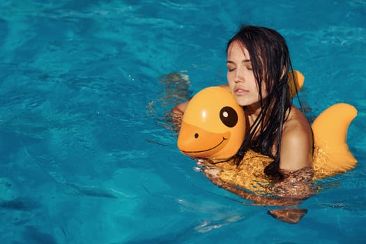 With yellow duck toy. Girl have fun and rest in swimming pool at daytime. Conception of vacation.