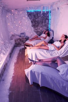 Young women in white towels lying down on beds indoor in room with violet decor.