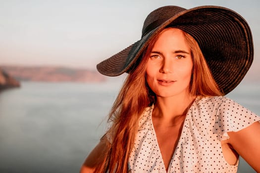 Portrait of happy young woman wearing summer black hat with large brim at beach on sunset. Closeup face of attractive girl with black straw hat. Happy young woman smiling and looking at camera at sea