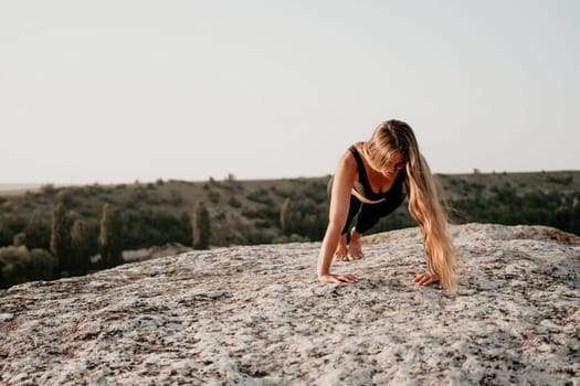 Well looking middle aged woman with long hair, fitness instructor in leggings and tops doing stretching and pilates on the rock near forest. Female fitness yoga routine concept. Healthy lifestyle.