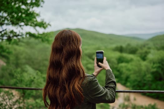 a woman in a raincoat takes pictures on the phone of a beautiful view of the forest. Travel, technology, mobile photography. High quality photo