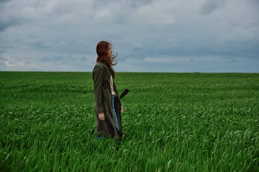 a beautiful woman stands in a green field in a raincoat and looks into the distance. Strong wind, flying hair, harmony with nature. High quality photo