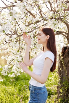 a pretty woman in casual clothes stands near a flowering tree in tall grass. High quality photo