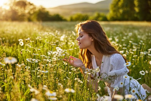 a beautiful woman in a light dress sits in a field of daisies against the backdrop of the setting sun and inhales their fragrance. High quality photo