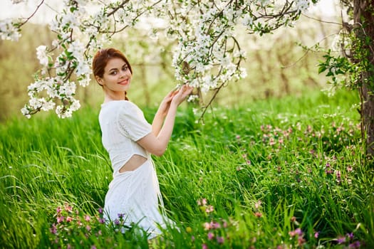 Beautiful woman in a blooming spring garden in a light dress smiling looking at the camera. High quality photo