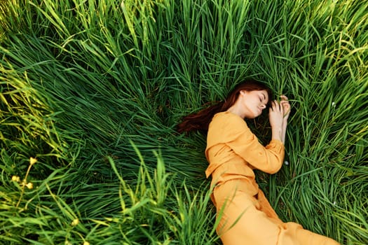 a relaxed woman enjoys summer lying in the tall green grass with her eyes closed. Photo taken from above. High quality photo