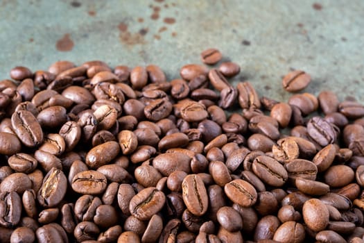 Close-up of roasted coffee beans on a green surface as a background. Selective focus.