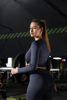 One adult caucasian woman female athlete putting weight plate on the barbel at gym. wearing blue leggins and long sleeve top