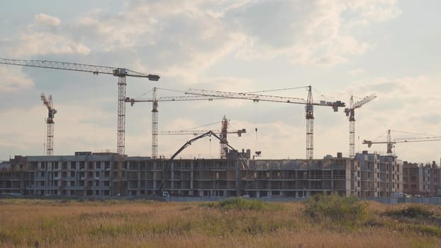 Silhouettes of construction cranes building a house in the evening