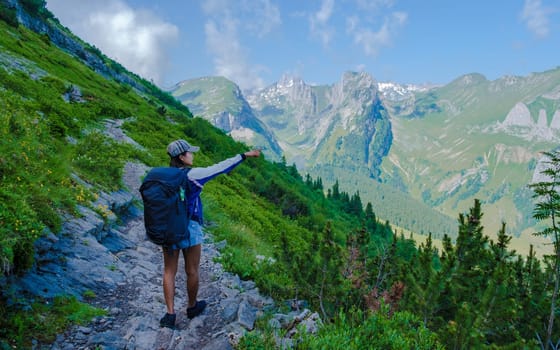 Asian women with hands up hiking in the Swiss Alps mountains during summer vacation with a backpack and hiking boots. woman walking on the Saxer Lucke path