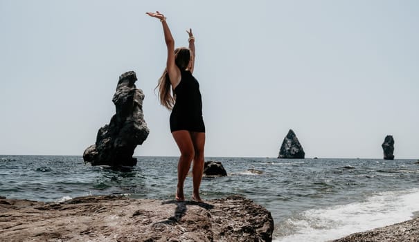 Woman travel sea. Young Happy woman in a long red dress posing on a beach near the sea on background of volcanic rocks, like in Iceland, sharing travel adventure journey