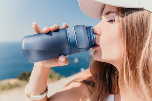 Fintess woman drinking water. Happy, active middle aged woman standing on beach and drinking water after excersise. Concept of lifestyle, sport. Close up.