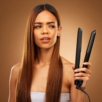 Hair, flat iron and confused woman in studio for beauty, wellness and keratin treatment on brown background. Hairdresser mockup, salon and girl with doubt for heat, haircare texture and cosmetics.
