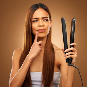 Hair, thinking and woman with flat iron for beauty, wellness and keratin treatment on brown background. Hairdresser mockup, salon and confused girl for healthy growth, haircare texture and cosmetics.