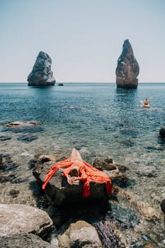 Woman travel sea. Young Happy woman in a long red dress posing on a beach near the sea on background of volcanic rocks, like in Iceland, sharing travel adventure journey