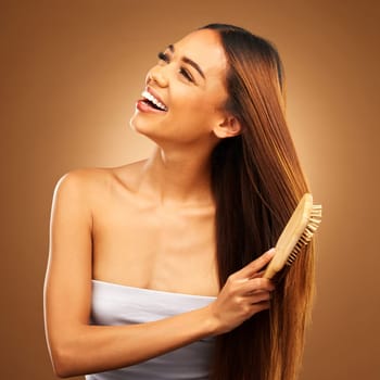 Brushing hair, beauty and a happy woman in studio for growth and color shine or healthy texture. Aesthetic female smile for brush, natural haircare and hairdresser or salon on brown background.