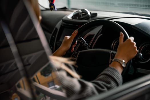 Fashion girl driving a car in a blue suit. Stylish woman sitting in the car and holding steering wheel. Shot through the side window.