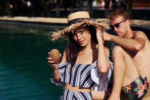 Holding drinks in hands. Cheerful couple or friends together in swimming pool at vacation.