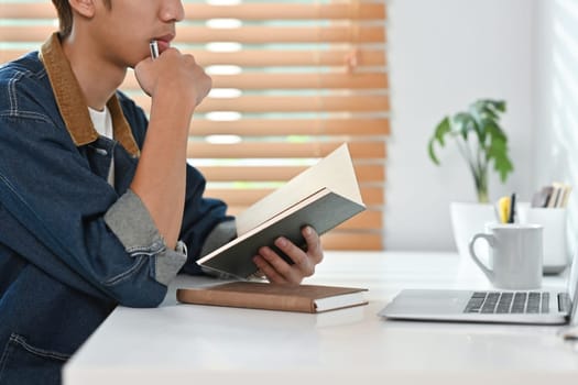 Stylish man holding notebook and working on laptop at home. Freelance, creative occupation, e-learning concept.