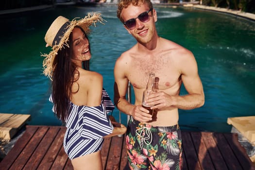 Holding drinks in hands. Cheerful couple or friends together in swimming pool at vacation.