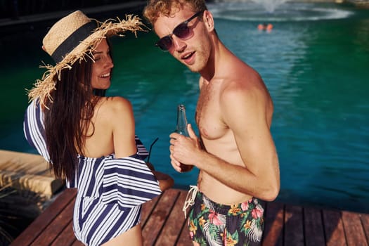 Holding drinks in hands. Cheerful couple or friends together in swimming pool at vacation.