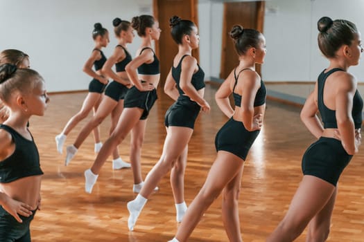 Group of female kids practicing athletic exercises together indoors.