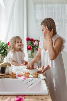 A little blonde girl with her mom on a kitchen countertop decorated with peonies. The concept of the relationship between mother and daughter. Spring atmosphere