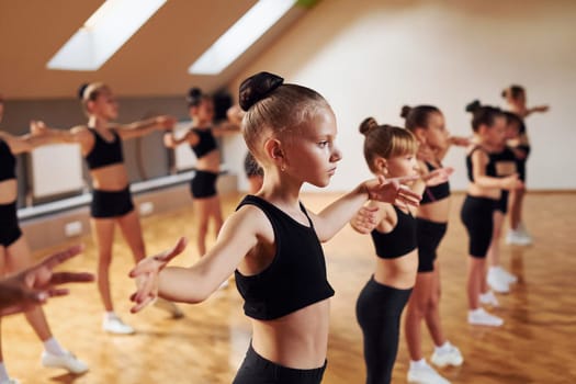 Standing in the row. Group of female kids practicing athletic exercises together indoors.