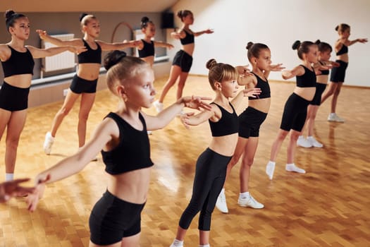 Standing in the row. Group of female kids practicing athletic exercises together indoors.