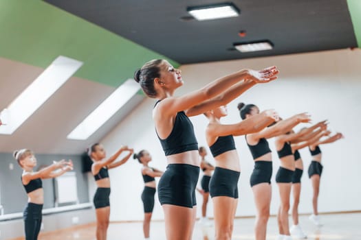 Standing and doing synchronised moves. Group of female kids practicing athletic exercises together indoors.