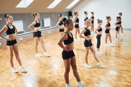 Side view of group of female kids that practicing athletic exercises together indoors.