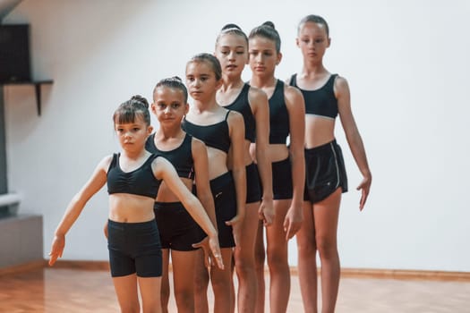 Daily routine. Group of female kids practicing athletic exercises together indoors.