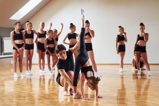 With help from coach. Group of female kids practicing athletic exercises together indoors.