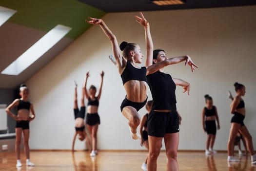 Woman teaching and helping. Group of female kids practicing athletic exercises together indoors.