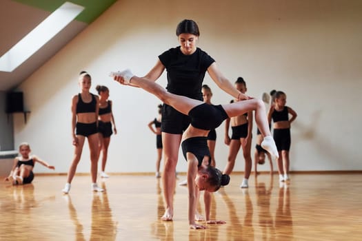 Woman teaching and helping. Group of female kids practicing athletic exercises together indoors.