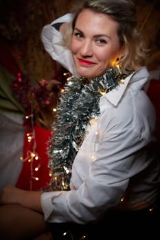 Portrait of a beautiful laughing funny blonde girl with light of garland on dark background before Christmas or New Year