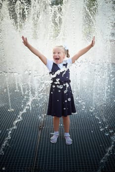 Little girl of elementary school student in modern school uniform outdoors near the fountain water jets. Female child schoolgirl having fun. Back to school in september 1